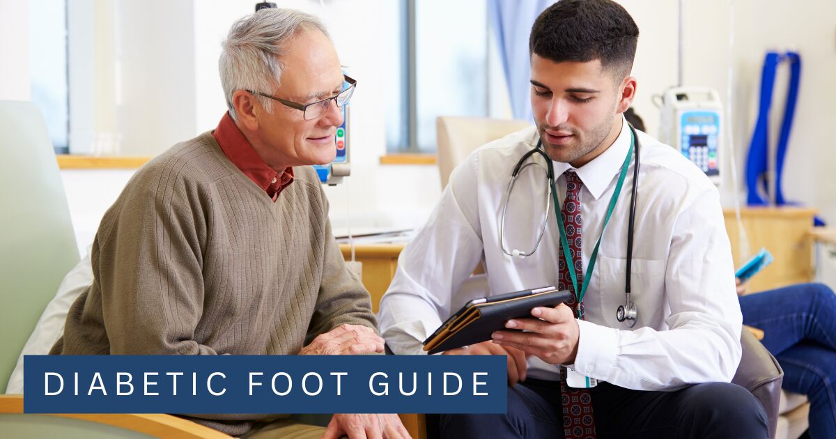 An older man in a clinic consultation with a clinician reviewing notes on a tablet